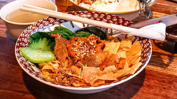 Canlı bir kase baharatlı kuru erişte sığır eti, yeşillik ve çıtır çıtır kraker üzerine soslu pirinç kasesi, yanında da kızarmış yumurta ve taze bir içecek..