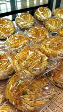 Yumuşak katmanlı altın hamur işleri bir fırında dokuma sepetinde sergilenen plastiğe sarılır. İkramlar hafif ışıklandırma altında parıldıyor, sabah müşterileri baştan çıkarıyor..