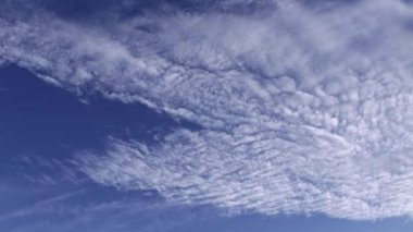 Beyaz ve gri, desenli sirrus ve iplikçik bulutlarının sinematik zaman çizelgesi güzel mavi gökyüzünde şişip dağılıyor.