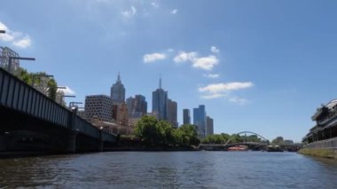 POV, Melbourne 'daki Yarra Nehri' nde güneşli bir günde gökdelenlerle birlikte süzülen bir kanonun 4K görüntüsünü taşıyor..