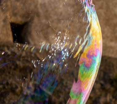 Snapshot of a large bubble with blue, pink, orange, green and yellow colours, popping, with the image of castle walls in the background clipart