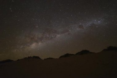 Wide field time lapse of milky way rotating across the night sky before being bathed in moonlight, casting a shadow across the sand dune tracks at moonrise. Western Australia