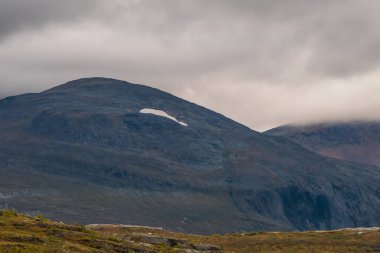 Kasvetli dağ manzarası. Dağda karlı bir nokta. Dağların tepesindeki bulutlar.
