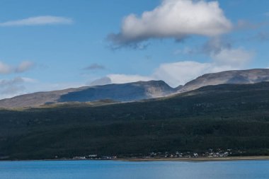 Deniz kıyısında küçük bir kasaba. Arka planda dağlar var. Dağdaki bulutların gölgeleri.