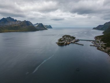 Norveç 'in Senja kentindeki Husoy balıkçı köyünün hava fotoğrafı. Kayalık dağlar ve bulutlu gökyüzü.