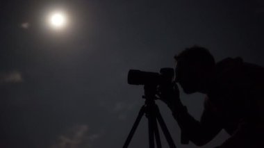 Man shooting the night cloudy sky under moon with a tripod