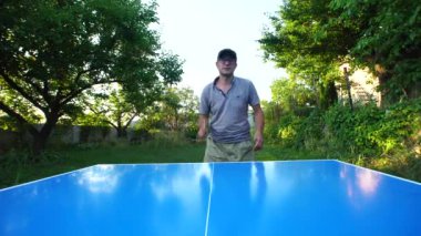 Man with glasses and a cap plays table tennis outdoors