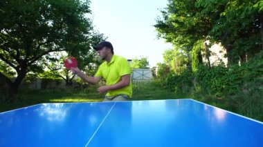Man with cap plays table tennis outdoors