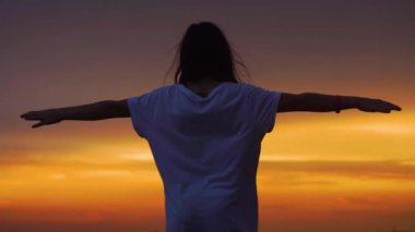 Silhouette of a girl with her arms raised to the sides against the backdrop of a beautiful sunset sky