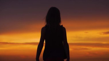 Silhouette of a girl with her arms raised to the sides against the backdrop of a beautiful sunset sky. Slow motion.