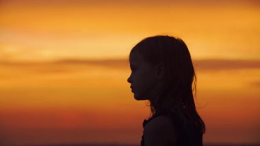 Silhouette closeup portrait of a adorable little girl against the backdrop of a beautiful sunset sky. 
