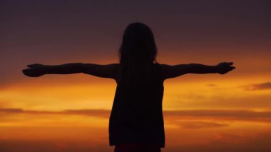 Silhouette of a girl with her arms raised to the sides against the backdrop of a beautiful sunset sky