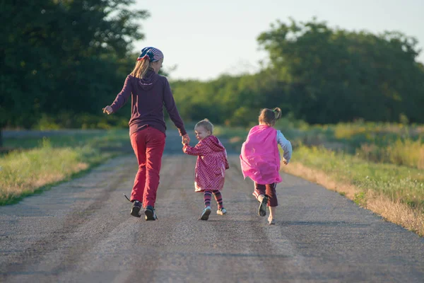 Mother and two children are running along the road countryside. Happy family.
