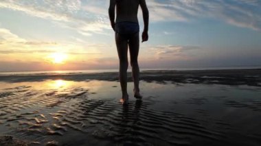 Çıplak ayaklı çocuk gün batımında kumlu deniz kıyısında yürüyor..
