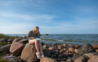 Güzel kız sahilde otururken eskizler çiziyor.