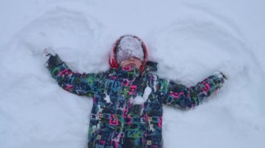 Çocuk karda yatarken bir kar meleği yapıyor..