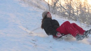 Mutlu kadın karlı bir yamaçta kızağa biniyor. Yavaş çekim