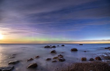 Şafakta bulutlu, yıldızlı bir gökyüzünün altında kayaları olan deniz manzarası..