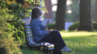 Güzel kız, batan güneşin altında bir bankta oturur..
