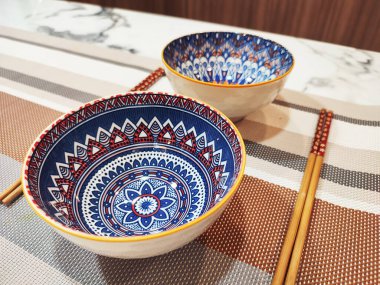 Mermer yemek masasının üstünde iki süslü seramik kase ve yemek çubuğu. Akdeniz motifli bir bowling topu. 45 derecelik açı..