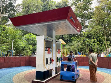 South Tangerang, Indonesia - May 10, 2024: Mother waiting for her children playing miniature gas station at Taman Kota 1 BSD public park. clipart