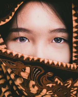 Kahverengi batik desenli sargıyla sarılmış bir kadının yüzü kontakt lenslerle kameraya bakarken gözlerini gösteriyor. Fotoğrafçılığı kapat.