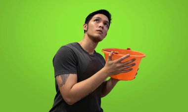 Tattooed person holding orange bucket, Wearing dark gray t-shirt isolated on bright green screen backdrop clipart