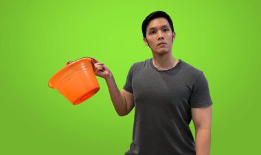 Person holding orange bucket with blank expression, Wearing dark gray t-shirt isolated on bright green screen backdrop clipart