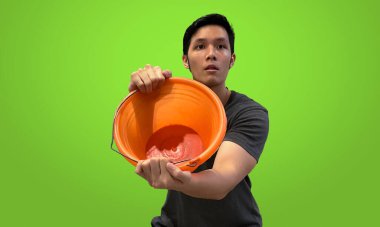 Man showing empty orange bucket to the camera, wearing casual outfit, isolated on vibrant green screen backdrop. clipart