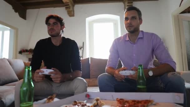 2人の友人は ピザを食べながら自宅でコンソールとビデオゲームをプレイし ビールを飲む — ストック動画