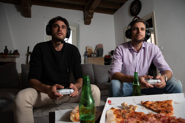 Concentrated friends playing hard and fast at video games with pizza and beer on the table.