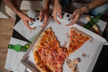 Oyun oynayıp pizza yiyen iki arkadaş..