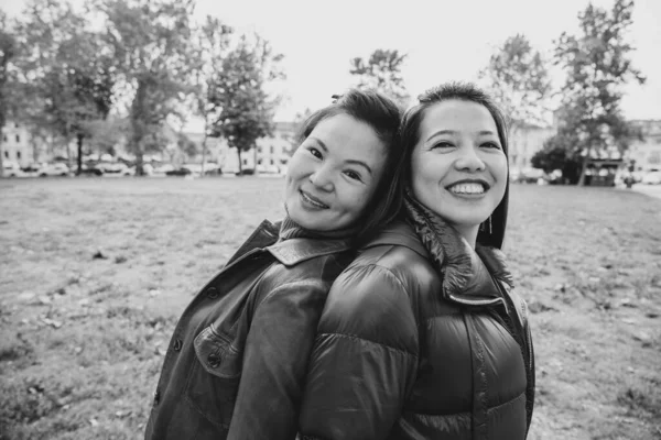 Black and white shot of two smiling chinese women leaning on their back.
