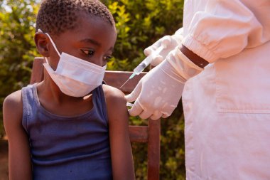 A little child wearing face mask sitting on a chair taking his injection. clipart