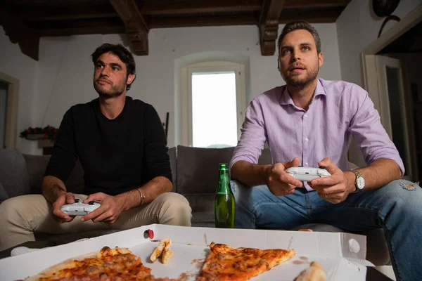 stock image Two young happy friends playing video games while sitting on the couch.