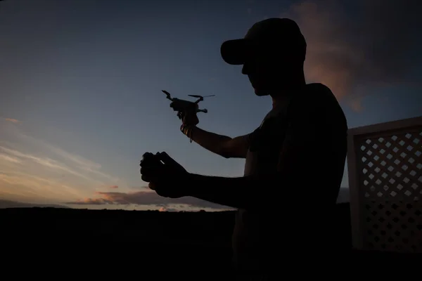 Silhouette of a drone pilot about to fly his drone during sunset