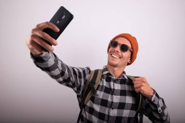 Genç gezgin çocuk gülümseyen bir selfie çekiyor, beyaz arkaplanlı bir stüdyo fotoğrafı.