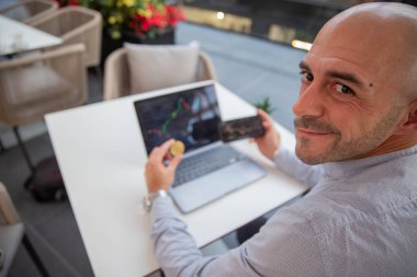 Elinde kripto para tutan memnun tüccar dizüstü bilgisayarı ve akıllı telefonuyla piyasayı kontrol ediyor.