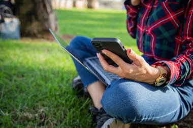 Close up of a girl's hands using her smartphone and laptop sitting in a public park