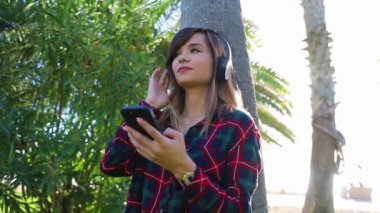 A girl enjoys music with her earphones and her smartphone in a public park
