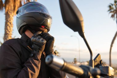 A motorcyclist puts on his helmet and fastens its belt, road safety concept