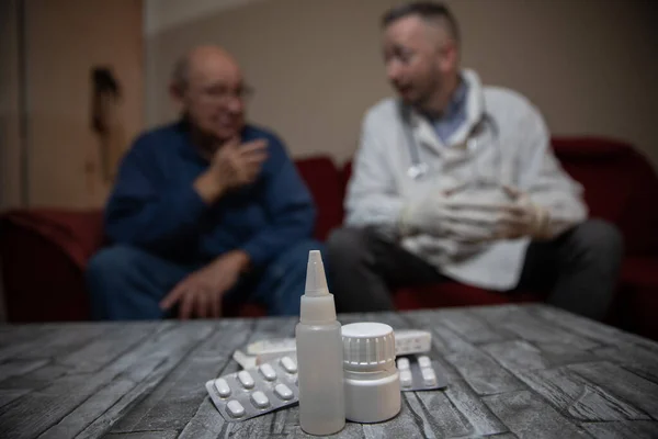 Close-up of medications on a table in an elderly patient's home during a doctor's visit.