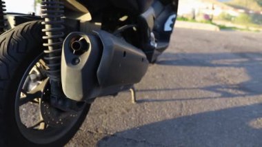 A motorcyclist gets on his scooter, close-up of the exhaust