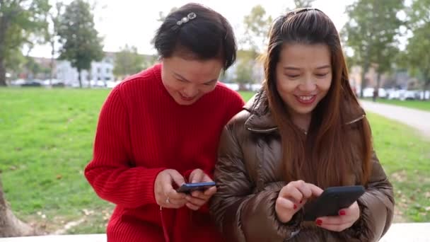Dwie Chinki Używają Swoich Smartfonów Siedząc Ławce Parku Publicznym — Wideo stockowe