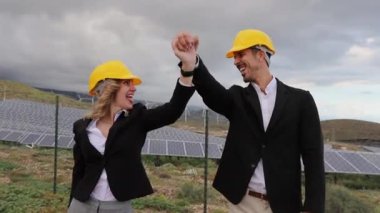Güneş enerjisi santralindeki iki mühendis silahlarını kaldırarak iş başarısını kutluyorlar.