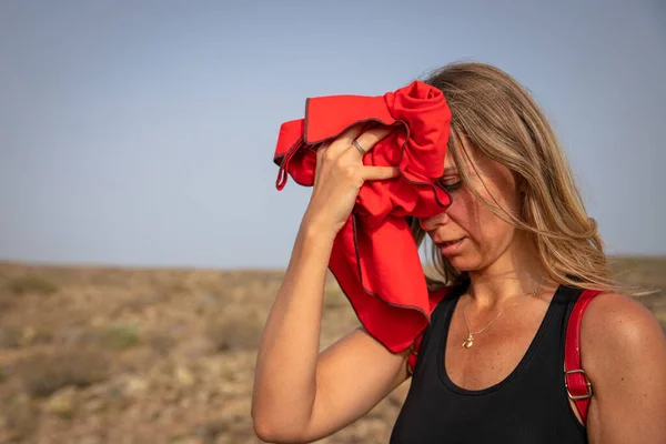 Bir kadın yürüyüşçü, terini bir havluyla yüzünden siler.