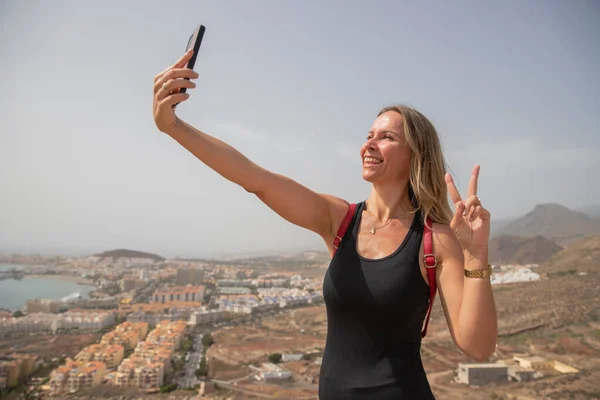 A female hiker takes a selfie smiling at the top of the mountain in summer