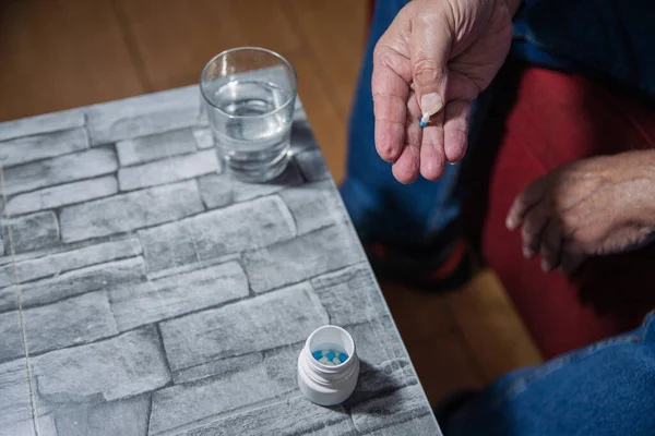 Hands of an elderly man taking medicine at home, he is holding a pill.