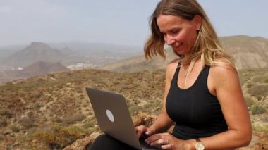 Yazın bir dağda yürüyüş yapan bir kadın dizüstü bilgisayarıyla çalışır.