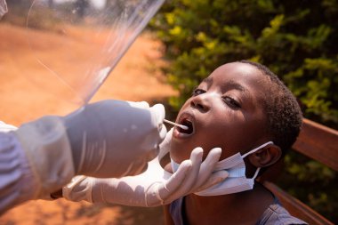 Bir doktor Afrika 'daki bir çocuğa koronavirüs testi yapar ve çubuğu boğazına sokar.